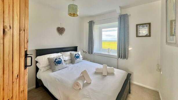 Een slaapkamer met een bed, kussens, een hanglamp, een raam met gordijnen en uitzicht op de omgeving.