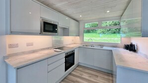 Una cocina moderna con armarios blancos, microondas integrado y ventana con vistas a un jardín.