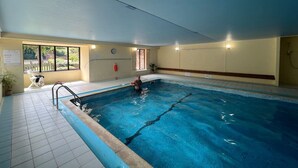 Ein Hallenbad mit gefliestem Boden, einer Metallleiter und einer Person, die schwimmt.