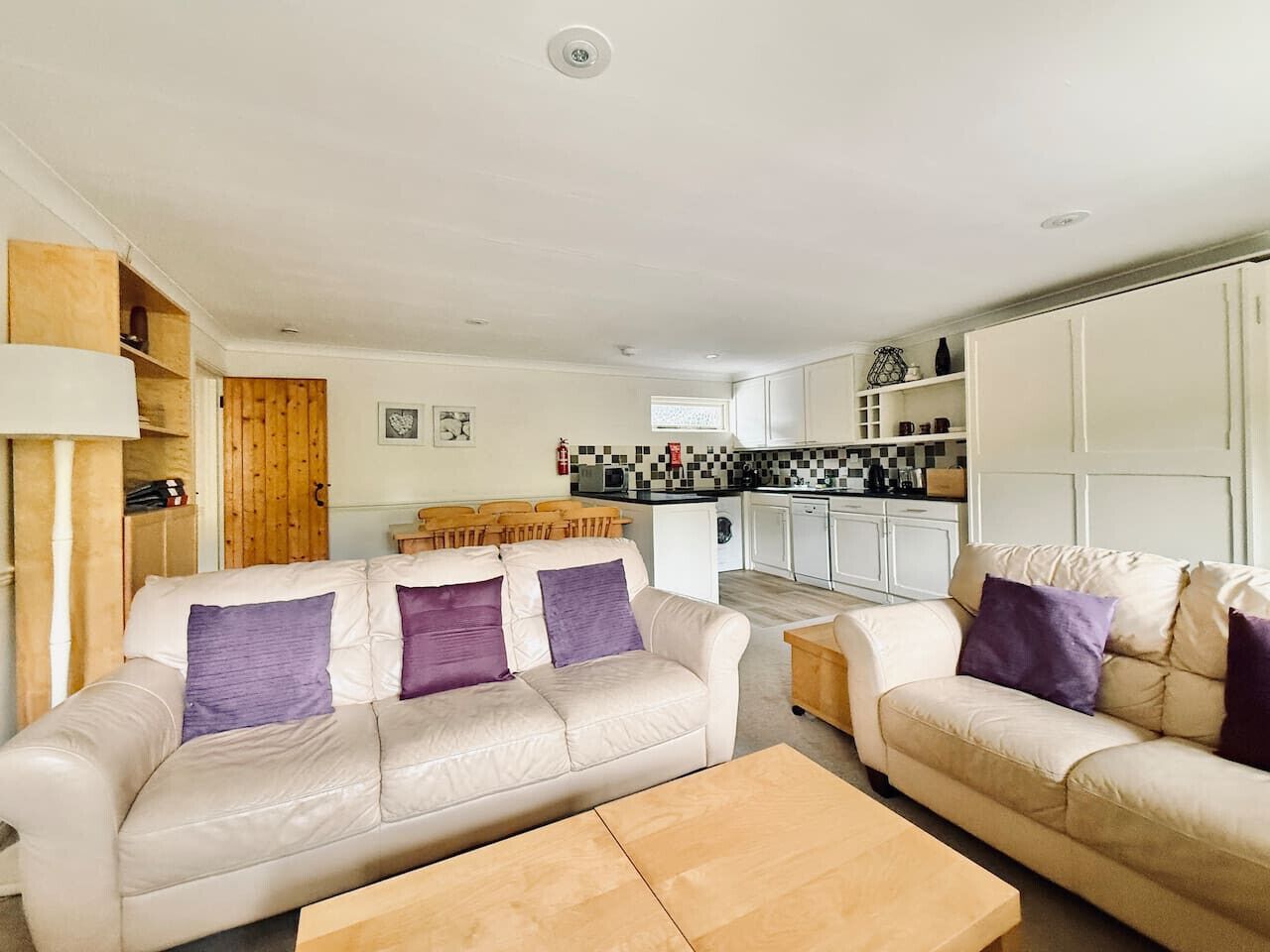 A living room with two beige sofas, a wooden coffee table, and a kitchen area in the background.