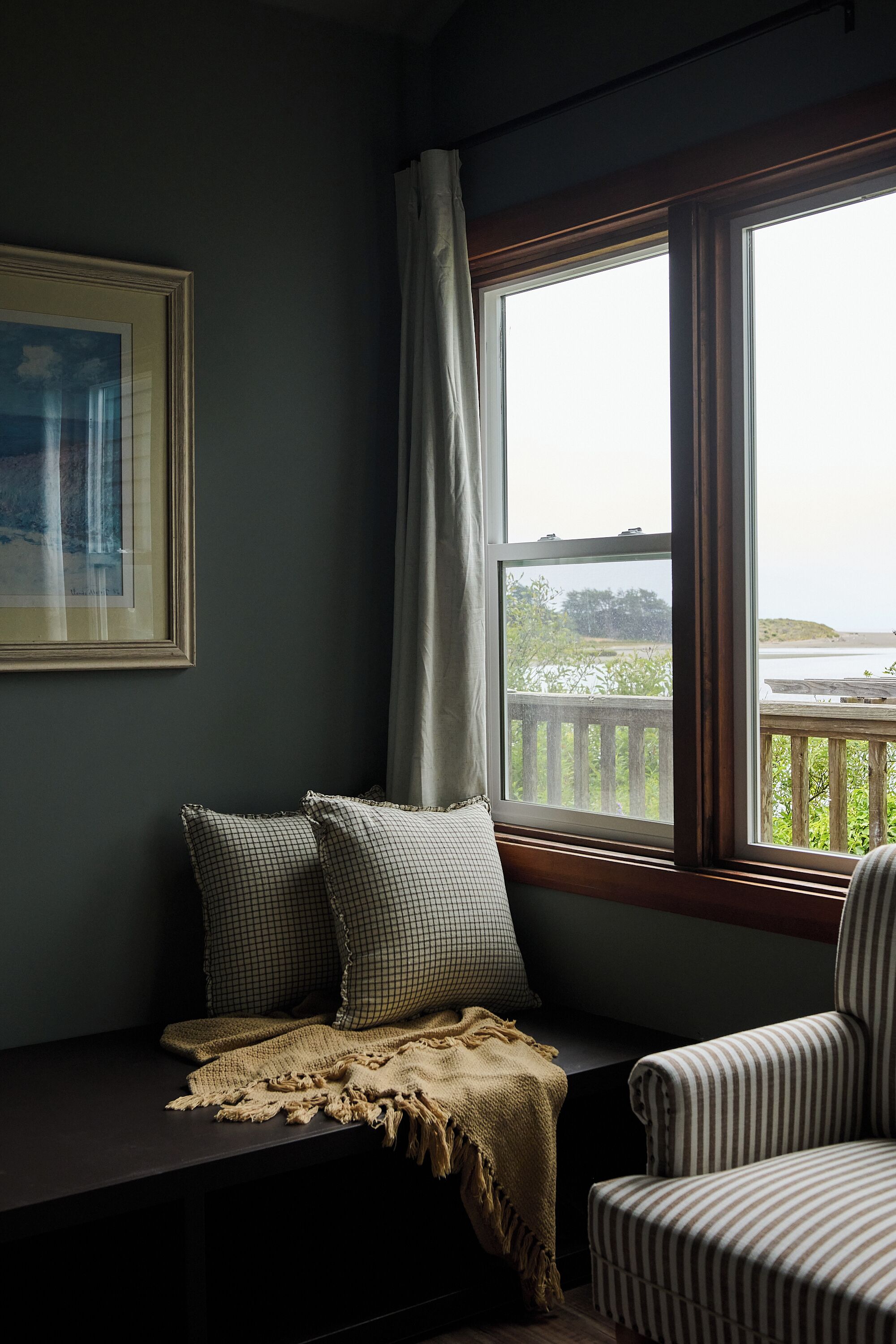 A corner seating area with a bench, a striped armchair, and a view of a balcony with a railing.