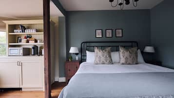 A bedroom with a bed, bedside tables, a nightstand, a dresser, a microwave, and a window.