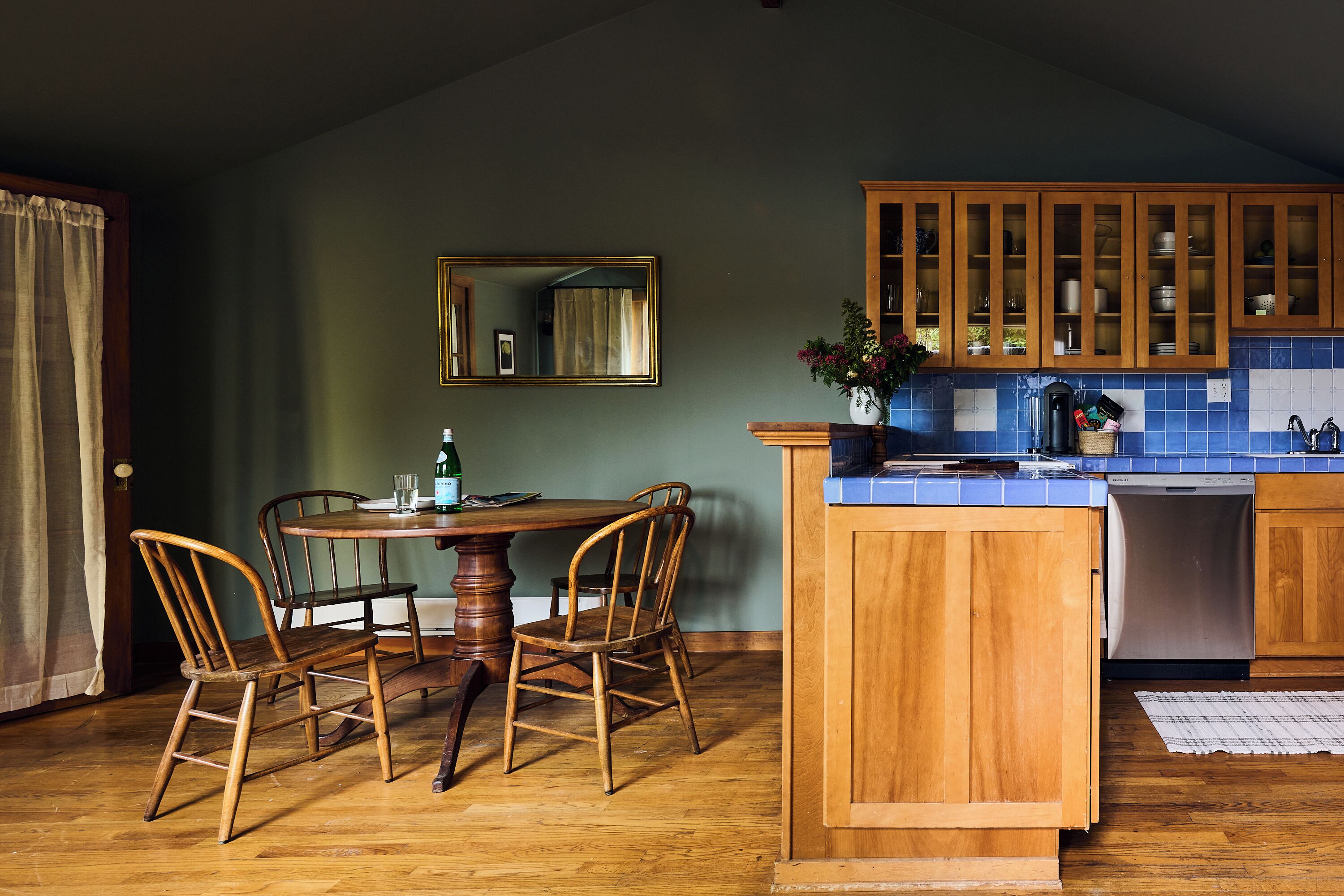 Een keuken met houten kastjes, een eettafel met stoelen en een inbouwvaatwasser.