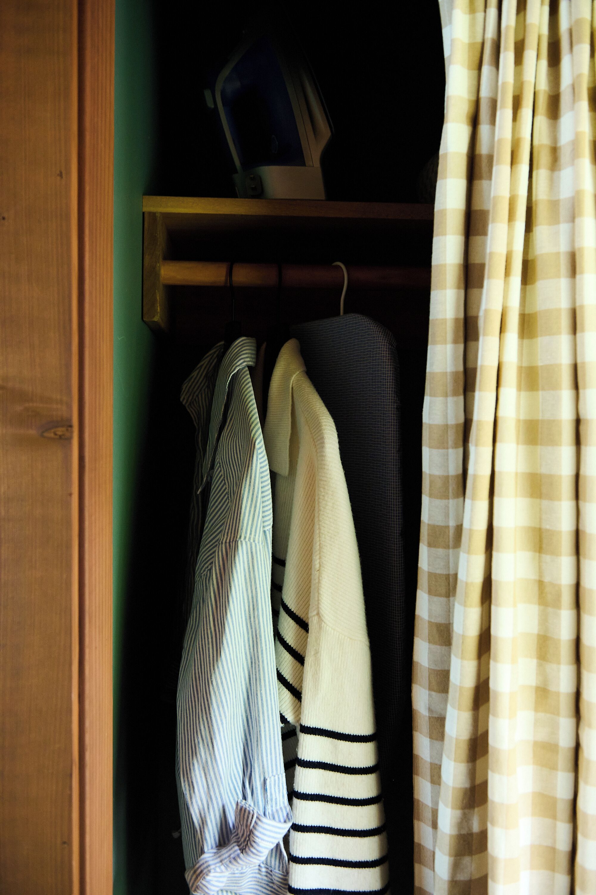 A wooden wardrobe with a hanging rack containing striped and solid-colored shirts.