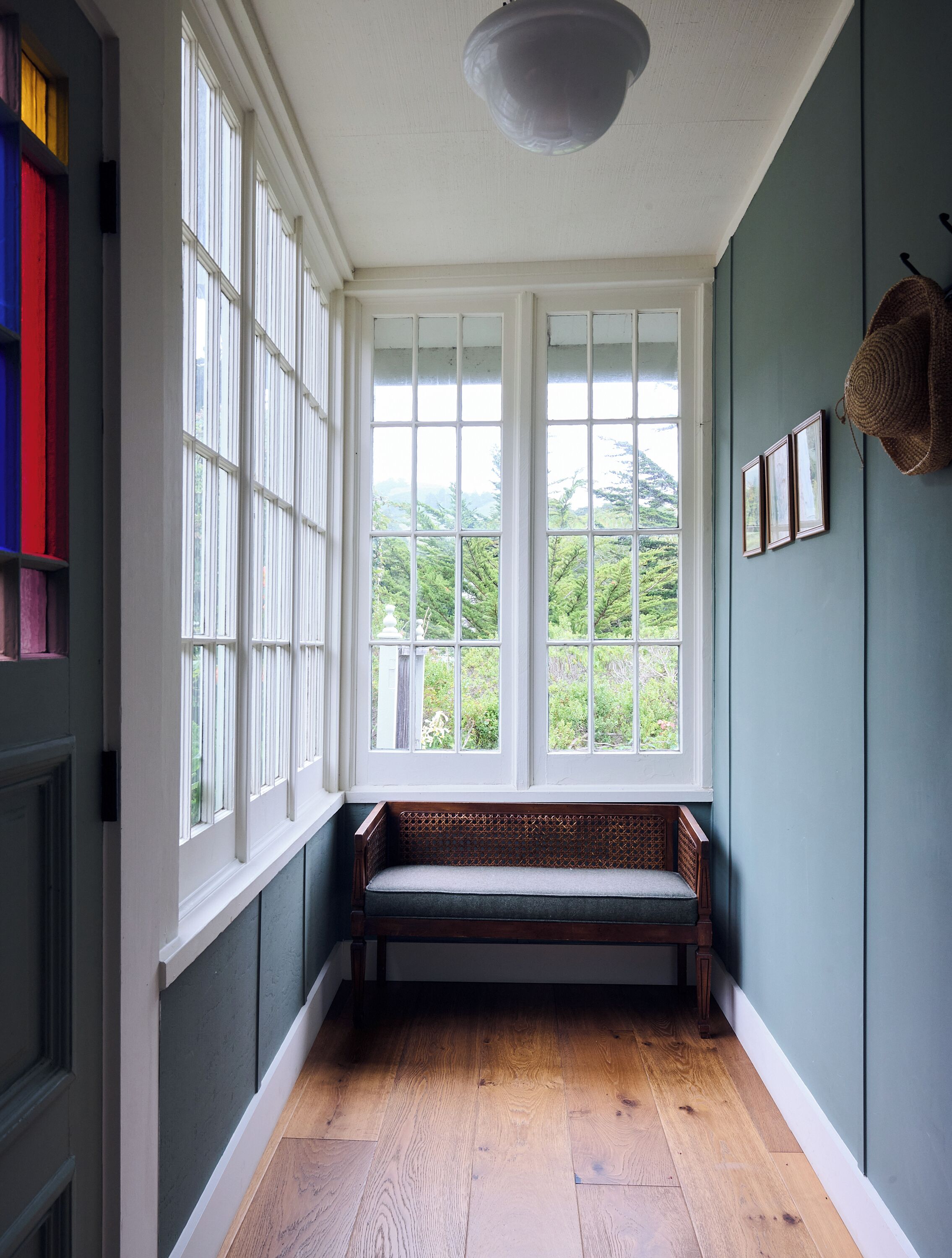 Ein Zimmer mit einer Sitzbank unter einem großen Fenster, einem an der Wand befestigten Hut und einer Deckenleuchte.