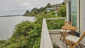 A wooden deck with a table and chairs overlooking a body of water, with houses in the background.