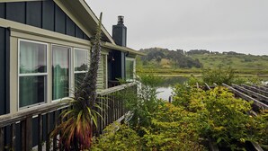 A house with a deck overlooking a lake, surrounded by greenery.