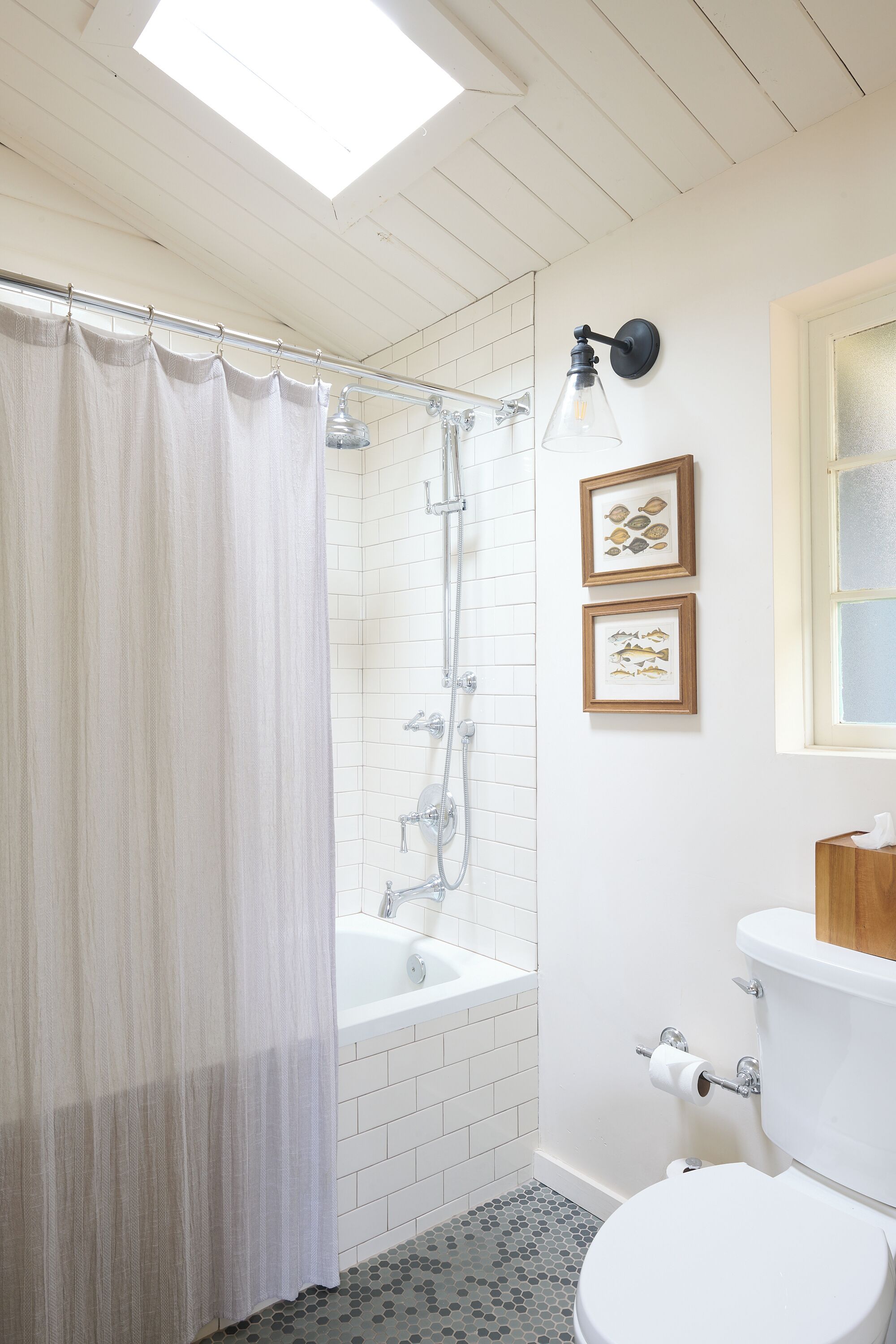 A bathroom with a shower curtain, a bathtub, a toilet, and two framed pictures on the wall.