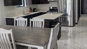 Une cuisine moderne avec des meubles de couleur sombre, des appareils en acier inoxydable, un comptoir en marbre et une table à manger en bois avec des chaises.