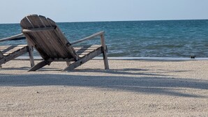 Une chaise de plage en bois, posée sur une plage de galets, d’où l’on a une vue dégagée sur l’océan.