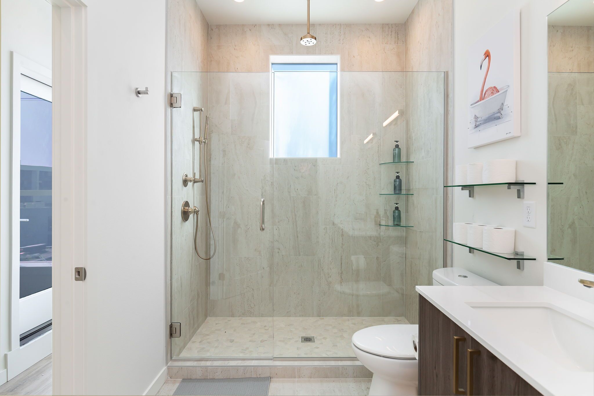 A modern bathroom with a glass-enclosed shower, a toilet, and a vanity with glass shelves.