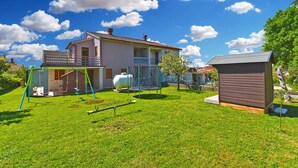 Ein Haus mit einem Garten, der eine Schaukel, ein Trampolin und einen Schuppen beinhaltet.