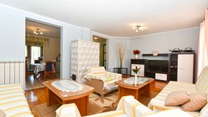 Ein Wohnzimmer mit einer Couch, zwei Sesseln, einem Couchtisch, einem Fernseher und einem Essbereich mit Tisch und Stühlen.
