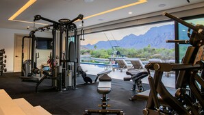 Un gimnasio con diversos equipos de ejercicio, una banca y vistas a montañas y un barco a través de amplias ventanas.