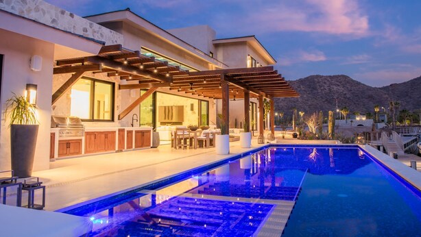 Un área de piscina moderna al aire libre con una pérgola, un bar y una zona de estar.