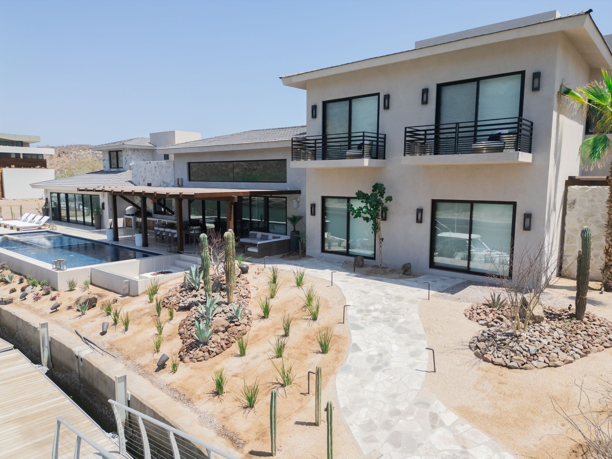 A modern two-story house with a swimming pool, outdoor seating area, and desert landscaping.