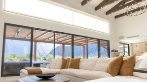 Una sala de estar moderna con un sofá seccional grande, una mesa redonda de centro y vistas a montañas a través de amplios ventanales.