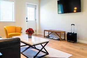 A living room with a sofa, a coffee table, a TV, and a suitcase. - SKKY Hotel (Whitehorse)