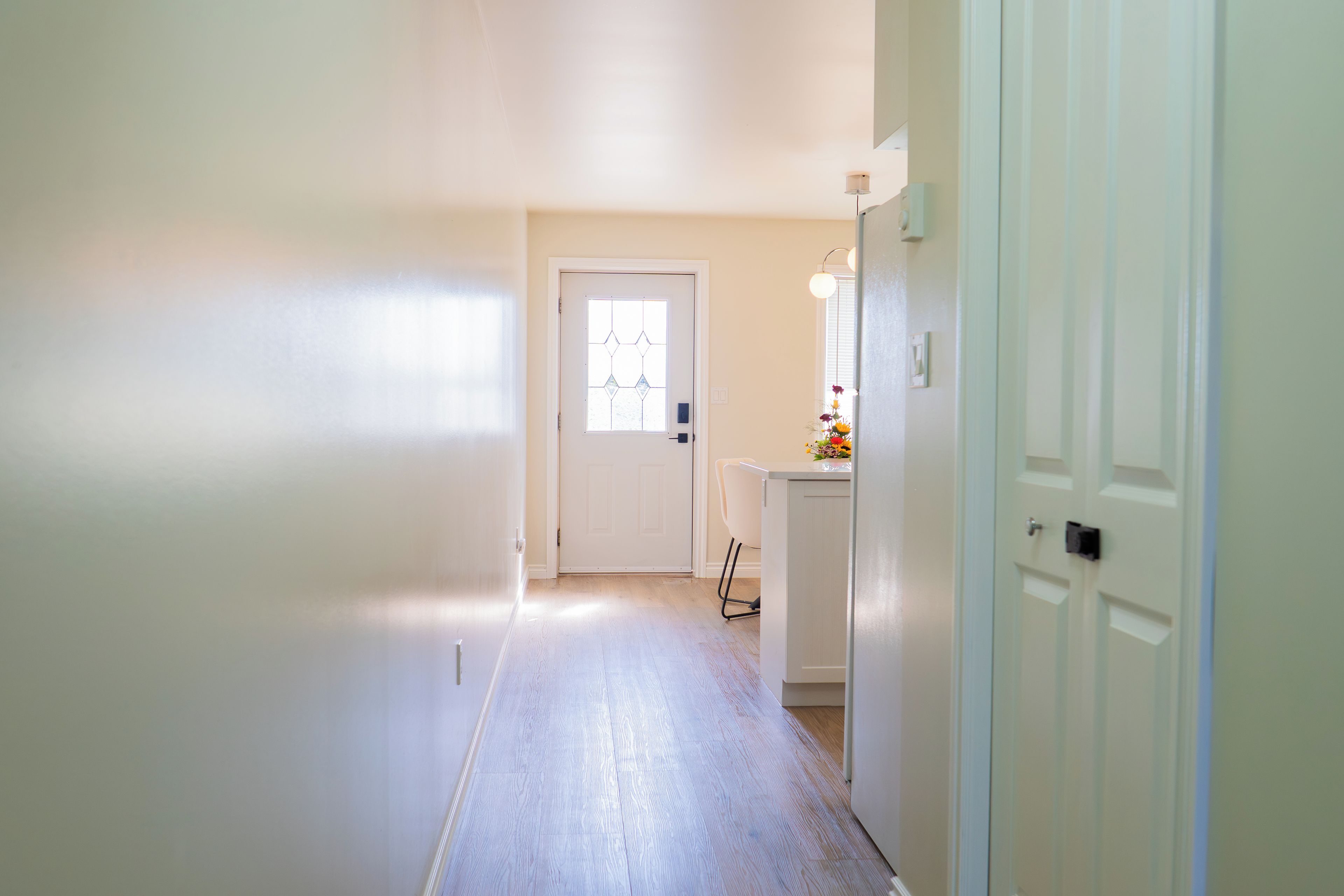 A hallway with a door at the end, a small table with a vase of flowers, and a chair.