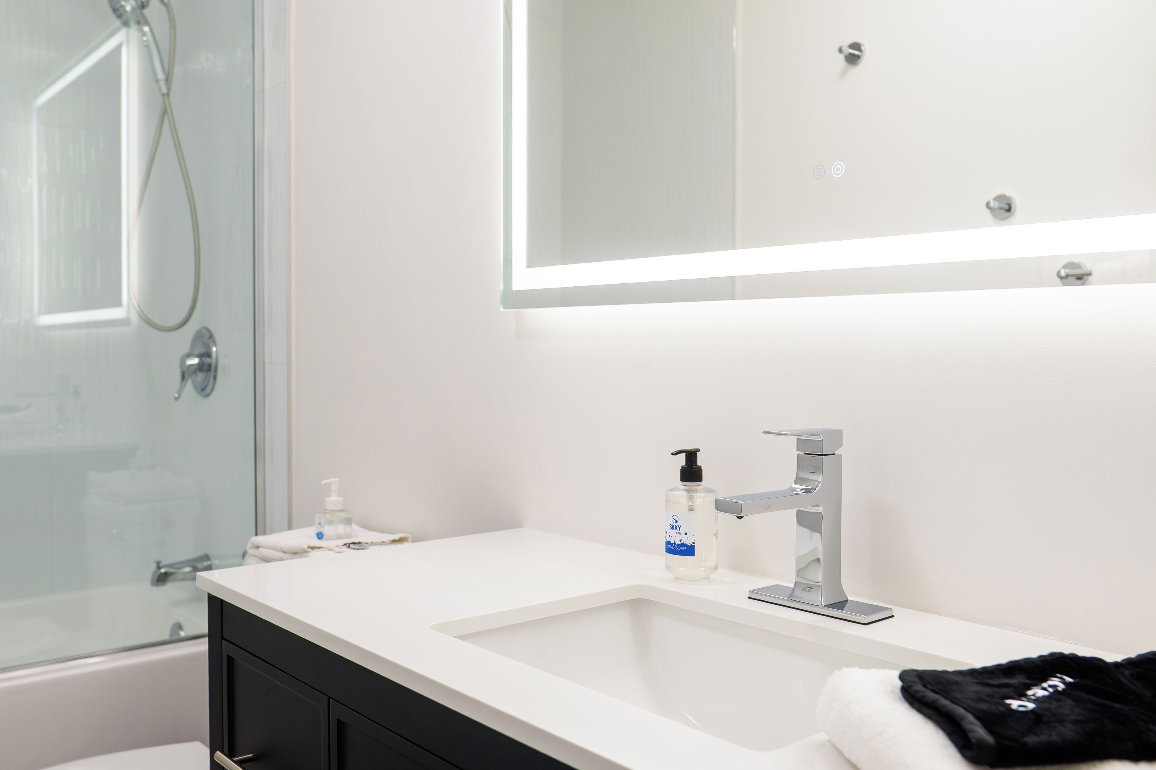 A modern bathroom with a glass shower enclosure, a white sink with a Delta faucet, and a mirror above the sink.