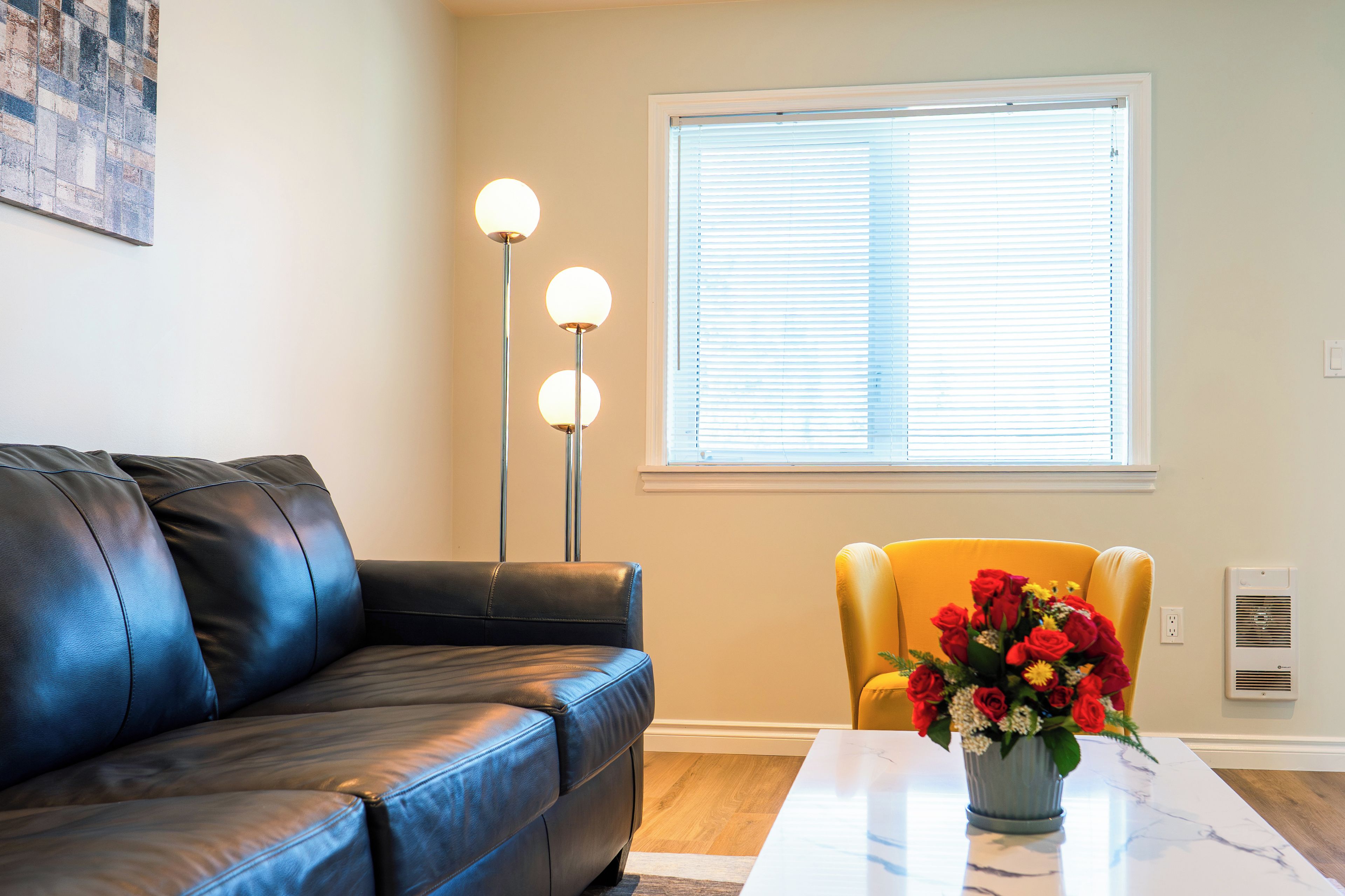 Una sala de estar con un sofá de cuero negro, un sillón amarillo, una mesa de centro blanca y un florero con flores.