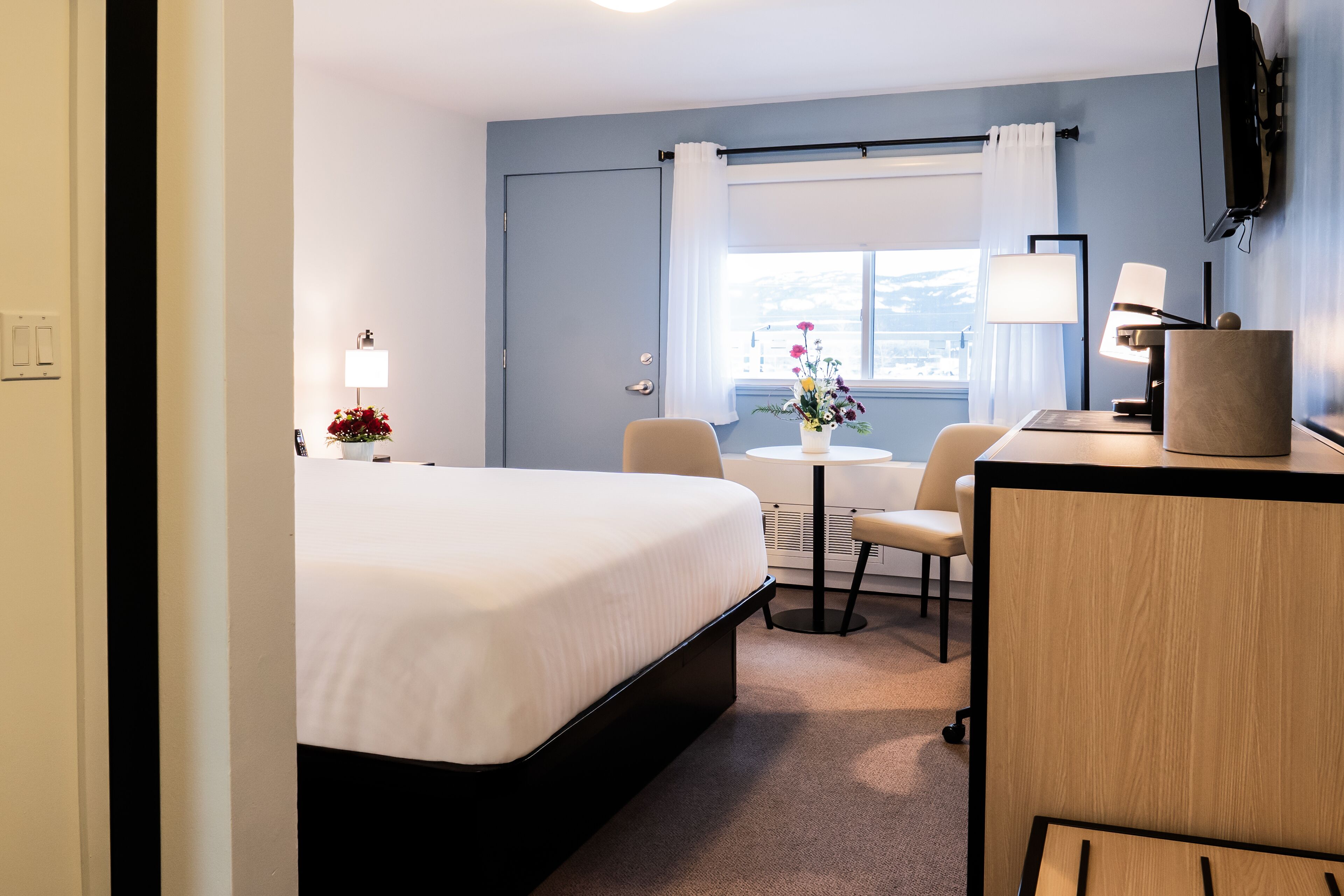Une chambre d’hôtel équipée d’un lit, d’un bureau, d’une chaise, d’une petite table, d’une lampe et d’un téléviseur.