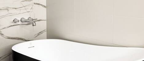 A modern bathroom with a freestanding black bathtub, marble wall tiles, and three framed pictures on the wall.