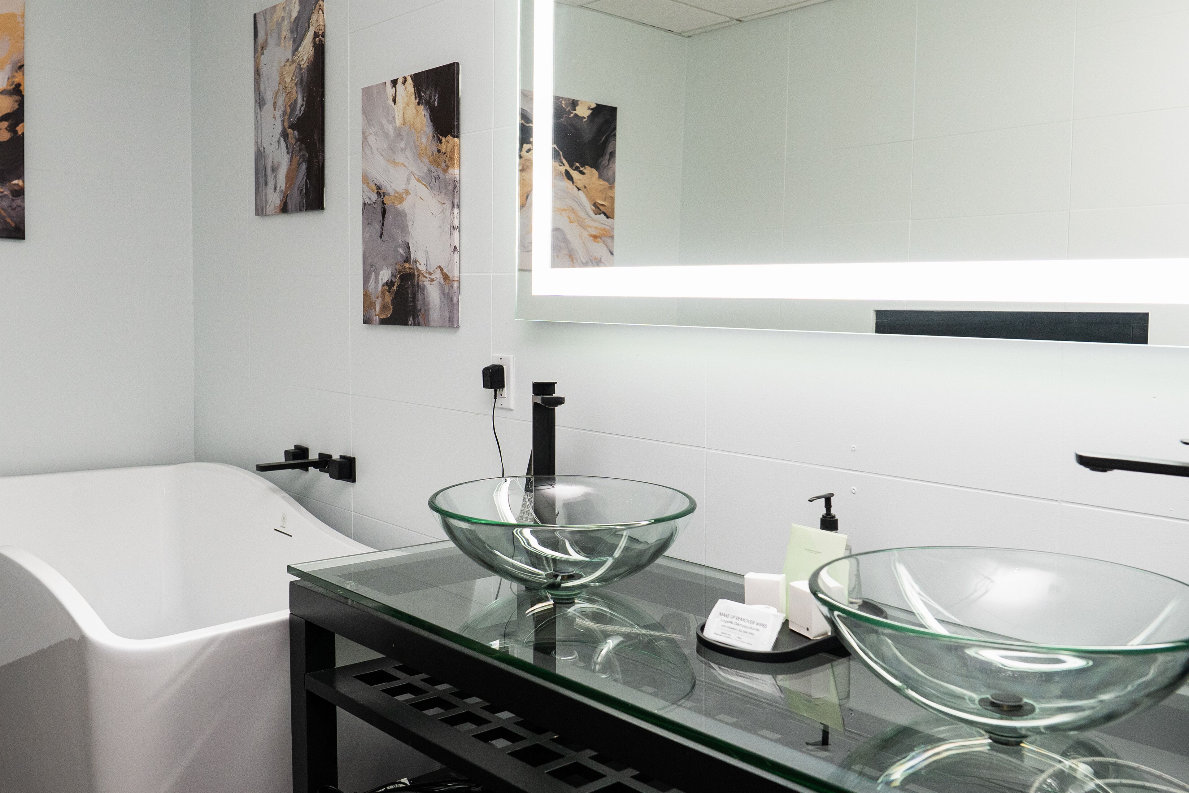 Une salle de bain moderne avec un lavabo en verre, un grand miroir et une baignoire blanche.