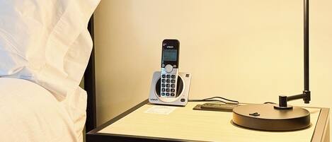 Een hotelkamer met nachtkastje, telefoon, lamp en een lade met een afstandsbediening.