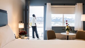 Habitación de hotel con cama, escritorio, silla, ventana con cortinas y vistas a montañas nevadas.