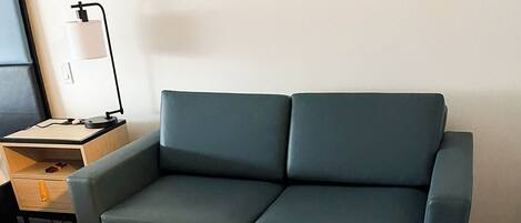 Un salon moderne avec un canapé bleu foncé, une petite table ronde sur laquelle est posé un menu, et un pouf jaune.