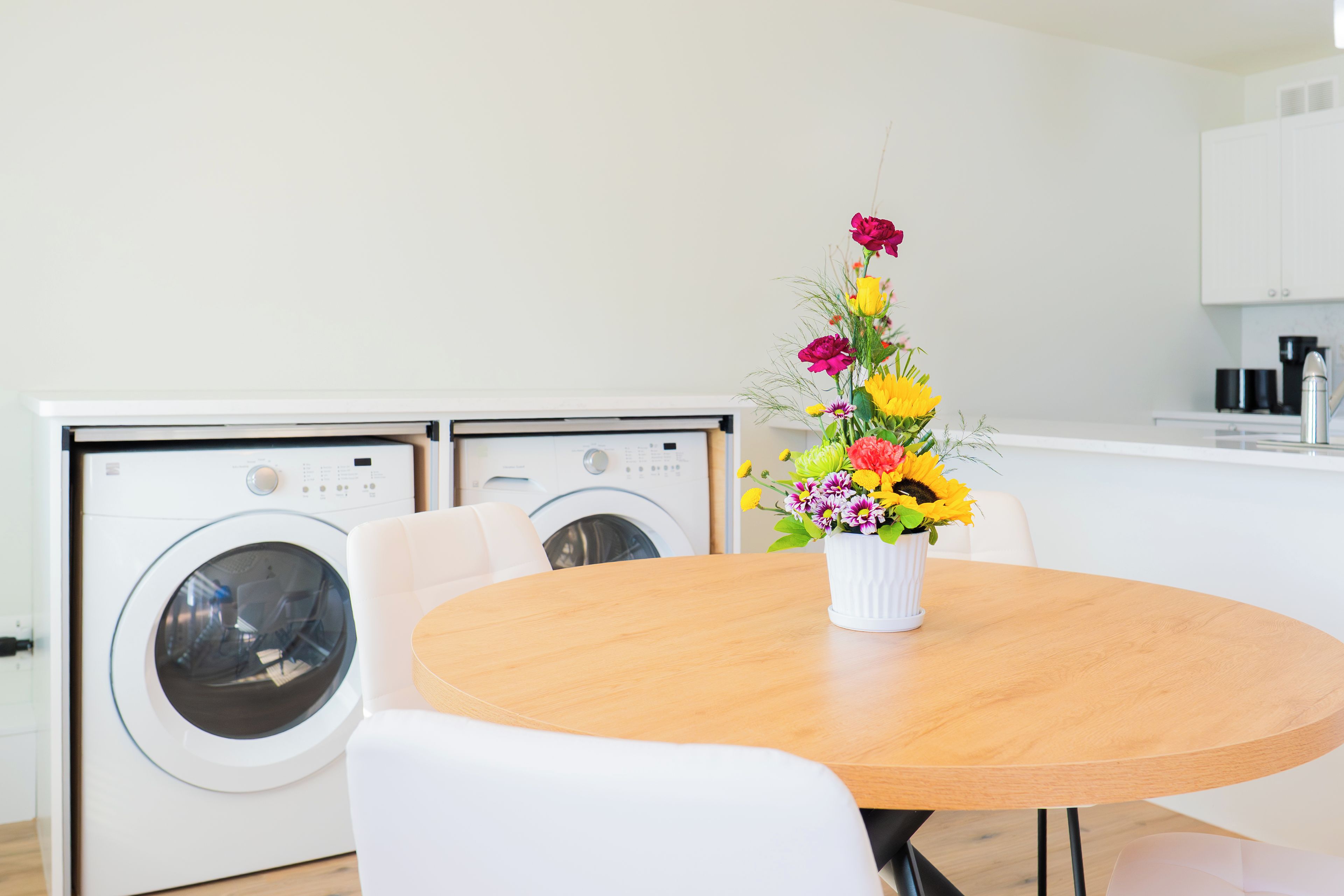 Une cuisine moderne avec des appareils électroménagers blancs, une table à manger en bois et un vase de fleurs.