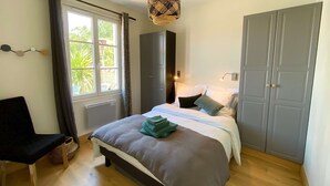 A bedroom with a bed, a chair, a wardrobe, and a window with curtains. - Beautiful  house in Loix (LOIX)