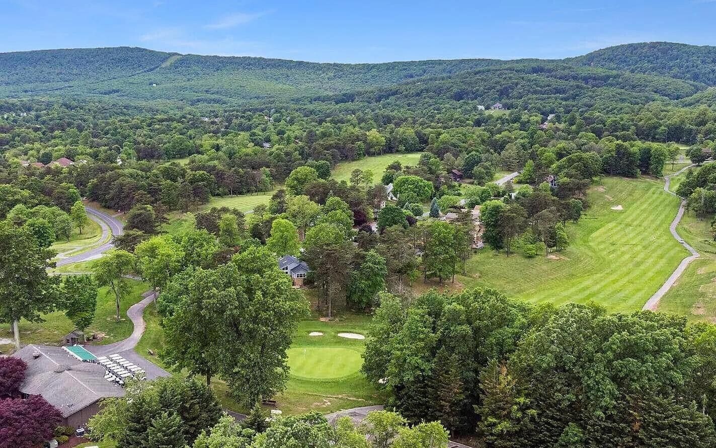 A golf course with a clubhouse, surrounded by dense forest and hills.