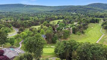 A golf course with a clubhouse, surrounded by dense forest and hills.
