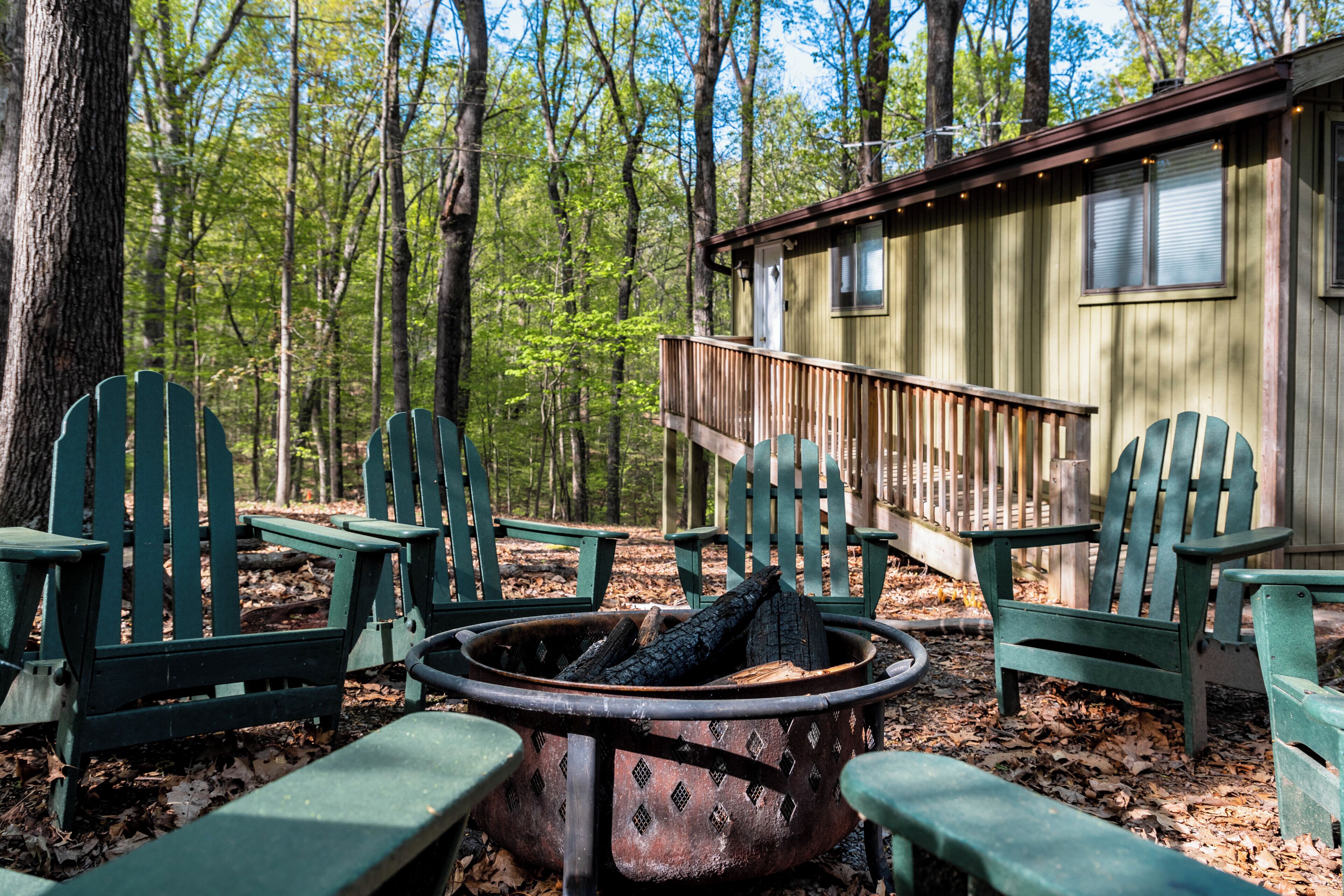 Una cabaña con terraza, rodeada de sillas Adirondack verdes y un pozo de fuego.