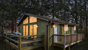 A wooden cabin with a deck and large windows, surrounded by trees.