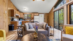 A modern kitchen with wooden cabinets, a dining area with a round table, and a living room with a sofa and a coffee table.