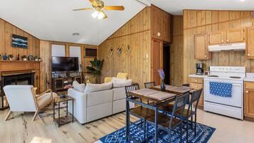 A modern kitchen with wooden cabinets, a dining area with a table and chairs, a sofa, and a television.