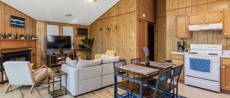 A modern kitchen with wooden cabinets, a dining area with a table and chairs, a sofa, and a television.