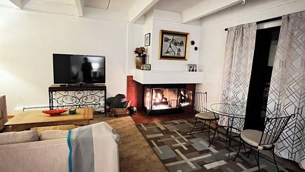 Een woonkamer met een bank, een televisie, een open haard en een eethoek met stoelen en een tafel.
