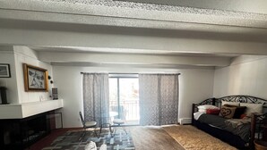 Een ruime woonkamer met een bank, een open haard, een eethoek met stoelen en een balkon met gordijnen.
