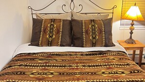 Een bed met een geborduurde spreidek, een metalen hoofdbord en een nachtkastje met een lamp.