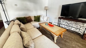 Een woonkamer met een beige modulaire bank, een houten salontafel, een flatscreen televisie en een decoratieve metalen standaard.