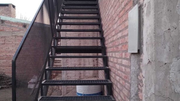 Un escalier en métal avec une rampe de protection en treillis menant à une porte.