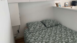Ein kleines Schlafzimmer mit einem Einzelbett, einem weißen Kleiderschrank und einem Regal mit Dekoration.