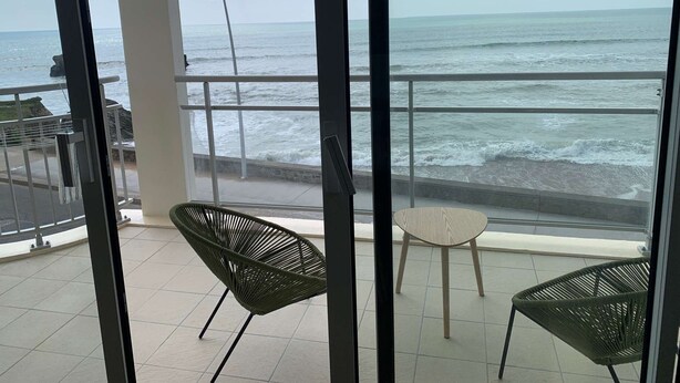 Ein Balkon mit Meerblick, zwei Stühle und ein kleiner Tisch.