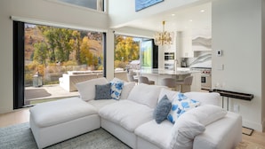 A modern living room with a white sectional sofa, a dining area, and a kitchen.