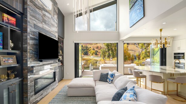 A modern living room with a fireplace, a large flat-screen TV, a white sofa, and a dining area with bar stools.