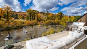 A balcony with a view of a river, a wooden deck, and a grill.